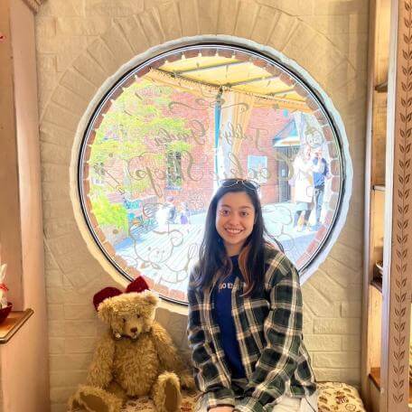 A woman sits on a bench, next to a toy teddy bear