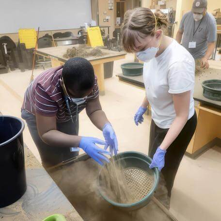 2 high schoolers with masks on, working with sand