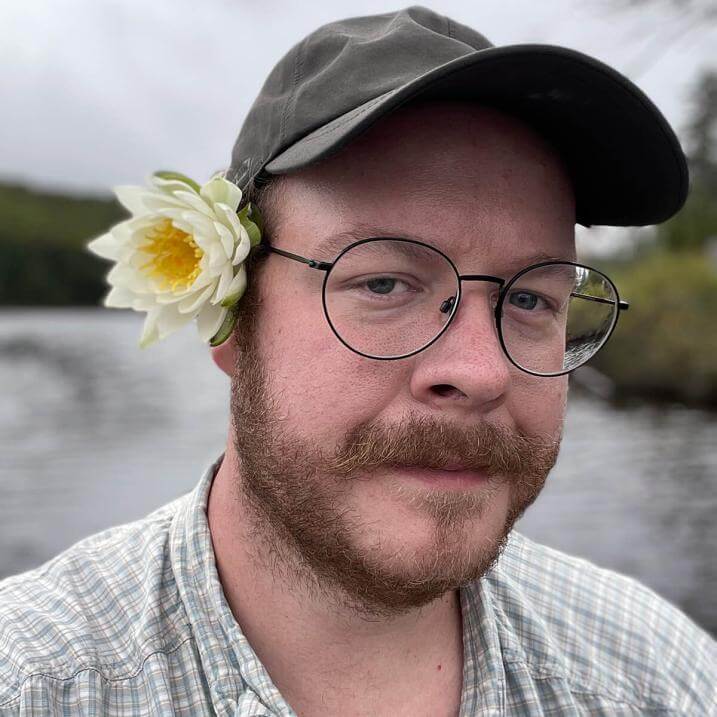 Andrew May outdoors with a cap on and a flower behind his ear