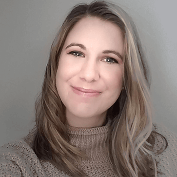 Nicole in portrait, smiling for the camera, against a soft gray background