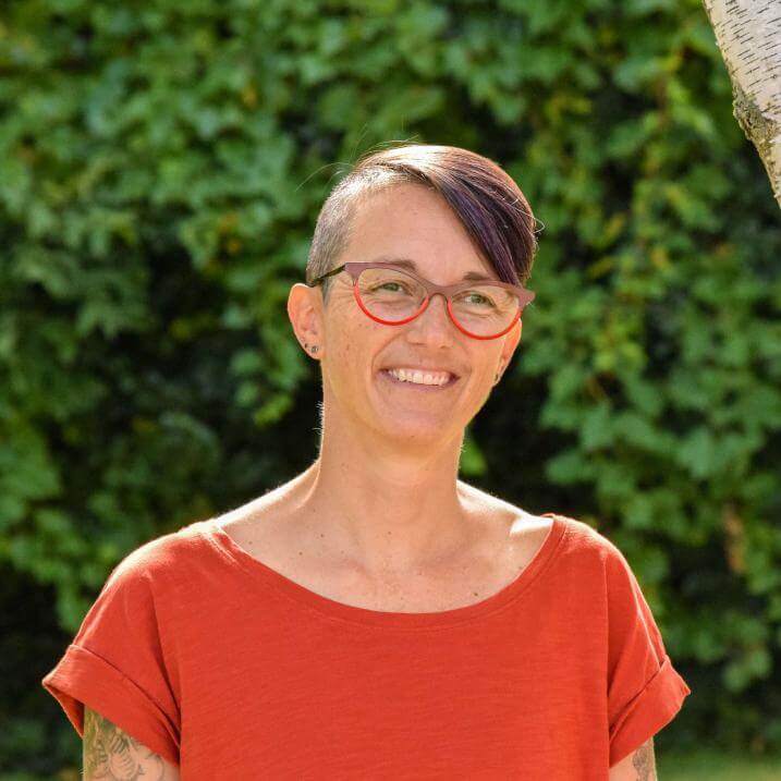 Kate Jerman smiling wearing a red shirt in front of greenery.