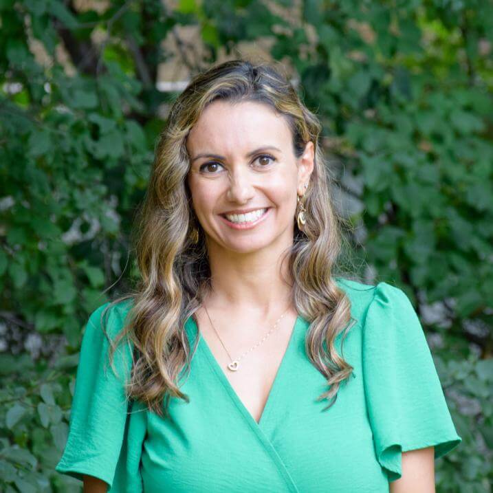 Michele Guyette smiling wearing a green dress standing in front of greenery.