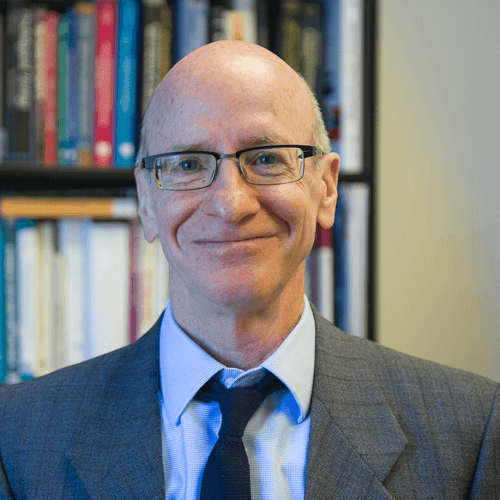 Tim, smiling, in an office type setting, with a book lined shelf behind him