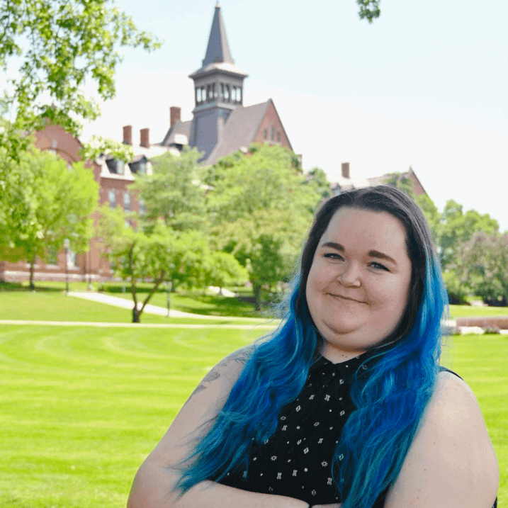 photo of Rachel K Norris, a person with blue hair standing in front of the UVM campus green