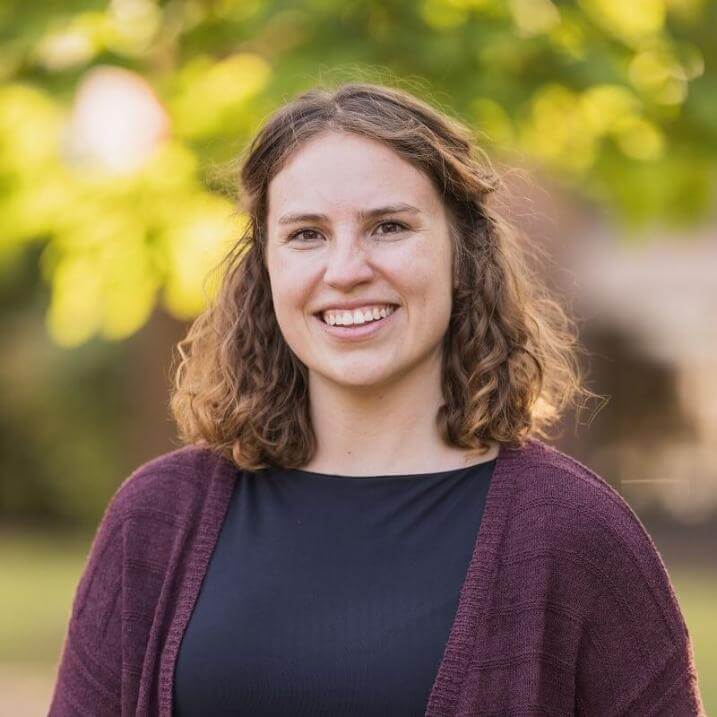 a headshot of a person in a black shirt with a maroon cardigan