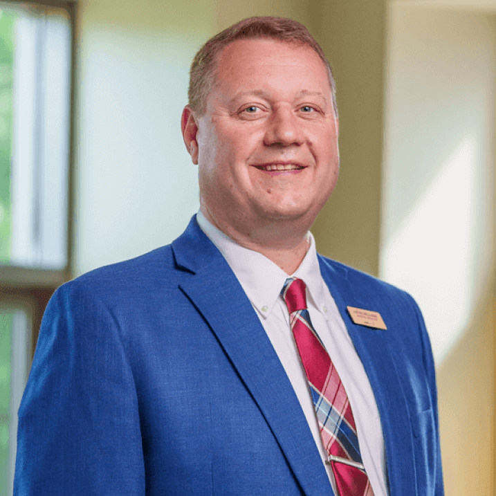 Director of Dining, Justin Dreslinski, stands smiling in a blue suit and tie