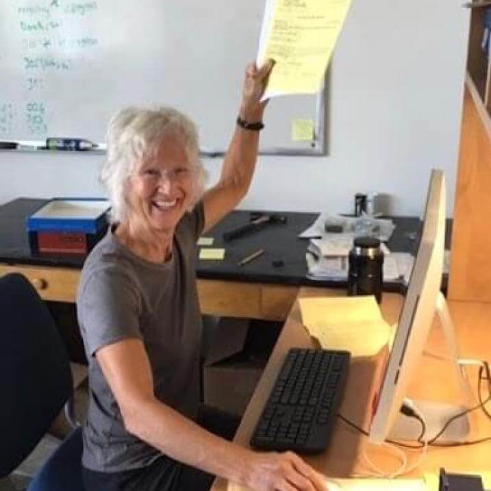Eunice smiling in front of a computer as she holds a paper aloft