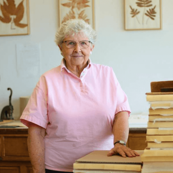 Hilda stands with her hand on a pile of specimens in the process of being mounted.