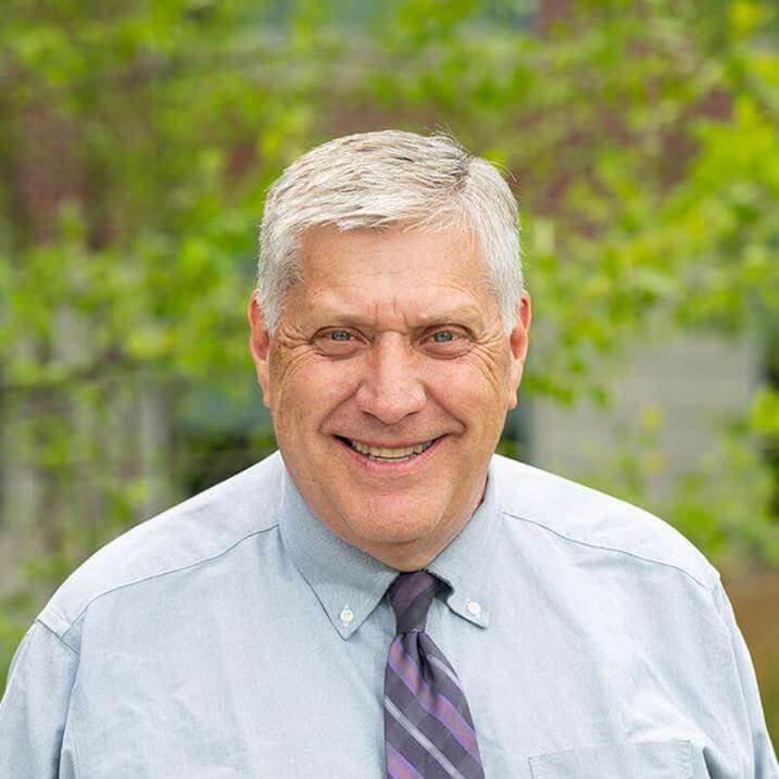 A person wearing a shirt and tie standing in front of a tree