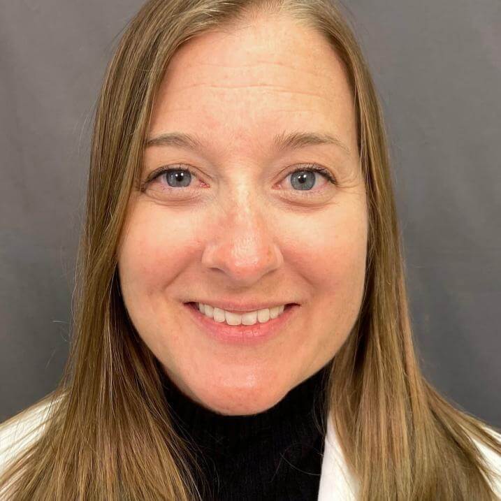 A person with long hair wearing a black shirt and a white coat