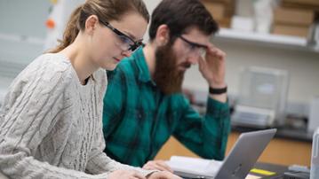 Two people engaged in work on laptops, surrounded by lab equipment in a well-lit laboratory environment