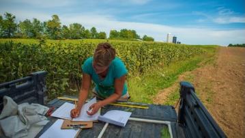A woman writes in a notebook in the bed of a pickup truck 