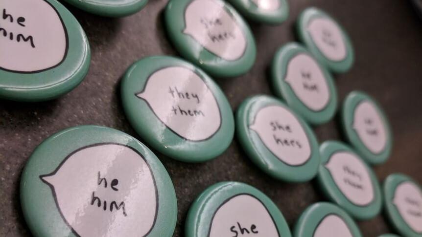 buttons with pronouns like he/him, she/her, they/them laid out on a flat surface