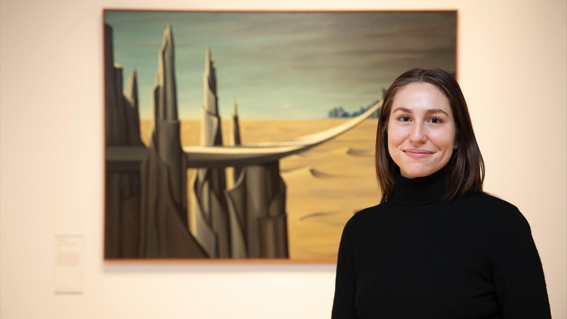 Alice Matthews '19 standing in front of beige wall with futuristic desert painting