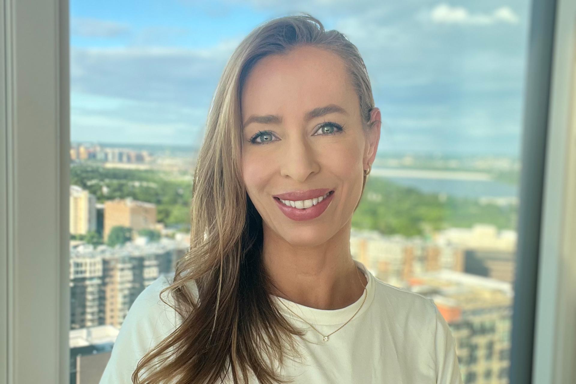 woman with long blond hair standing in front of window overlooking city