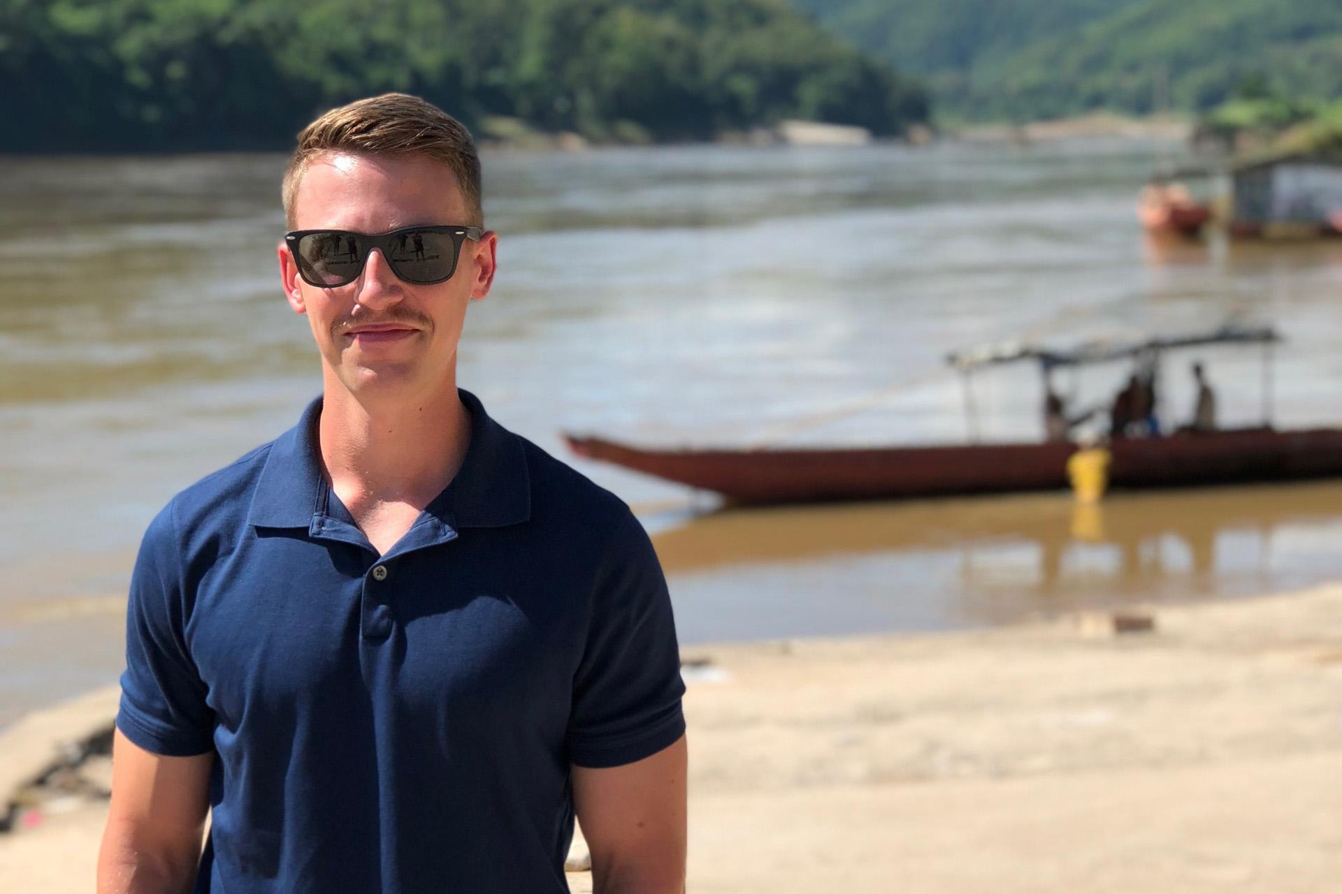 man in dark blue shirt and sunglasses standing on beach with boats in background