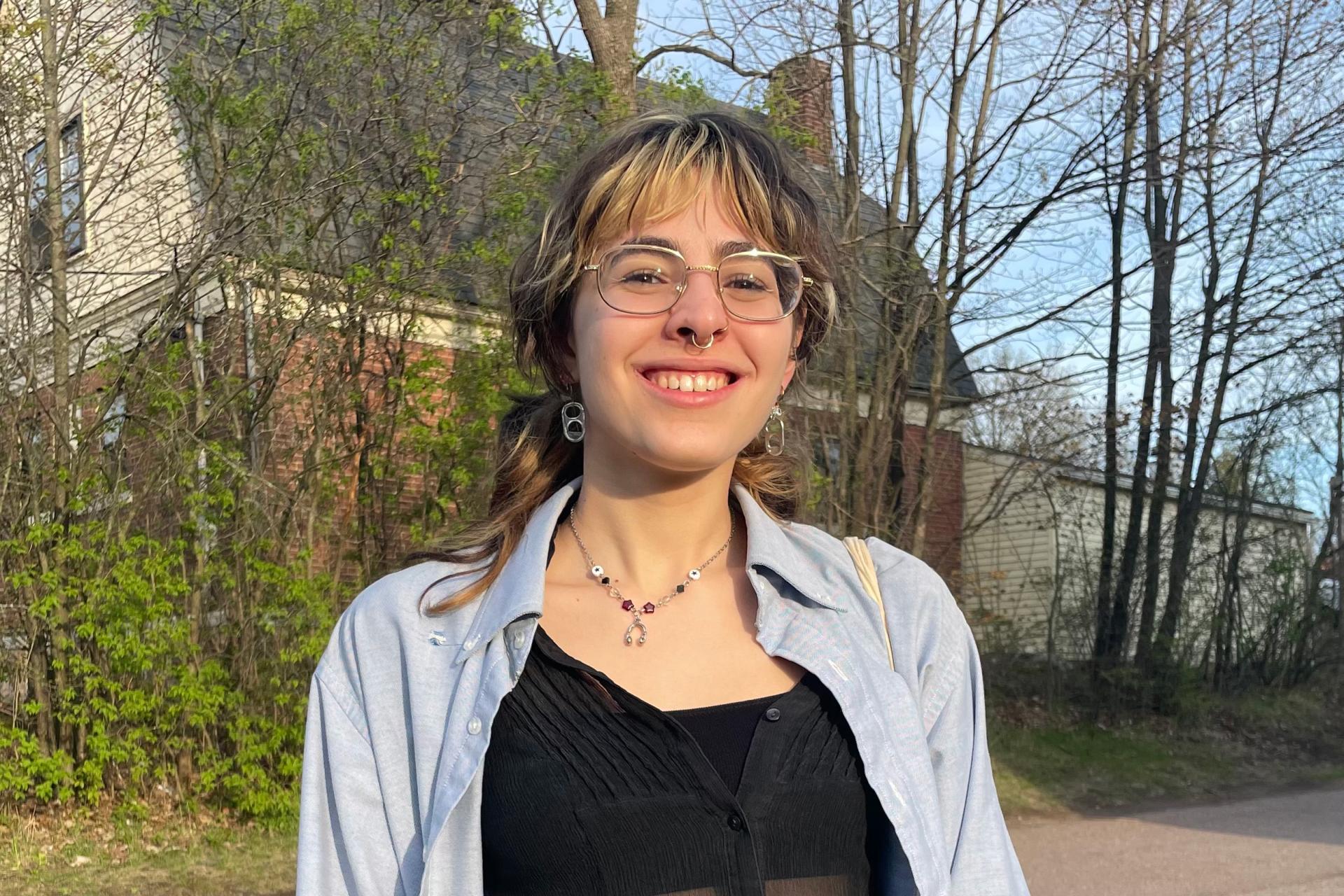 young woman with glasses and nose ring standing on street in front of house in early spring