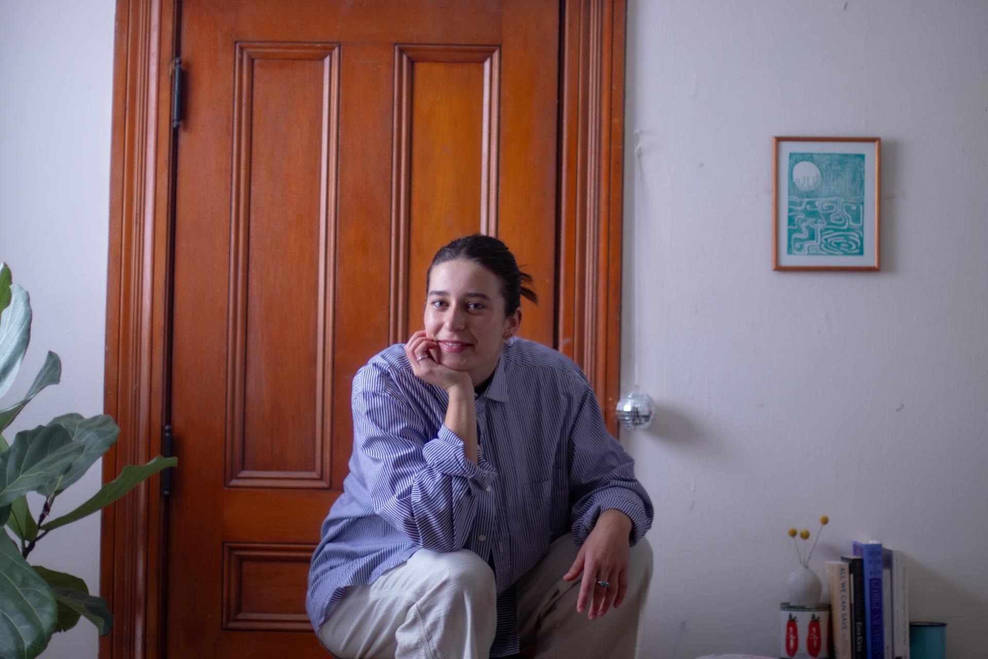 young woman crouched down with hand under chin in front of interior door