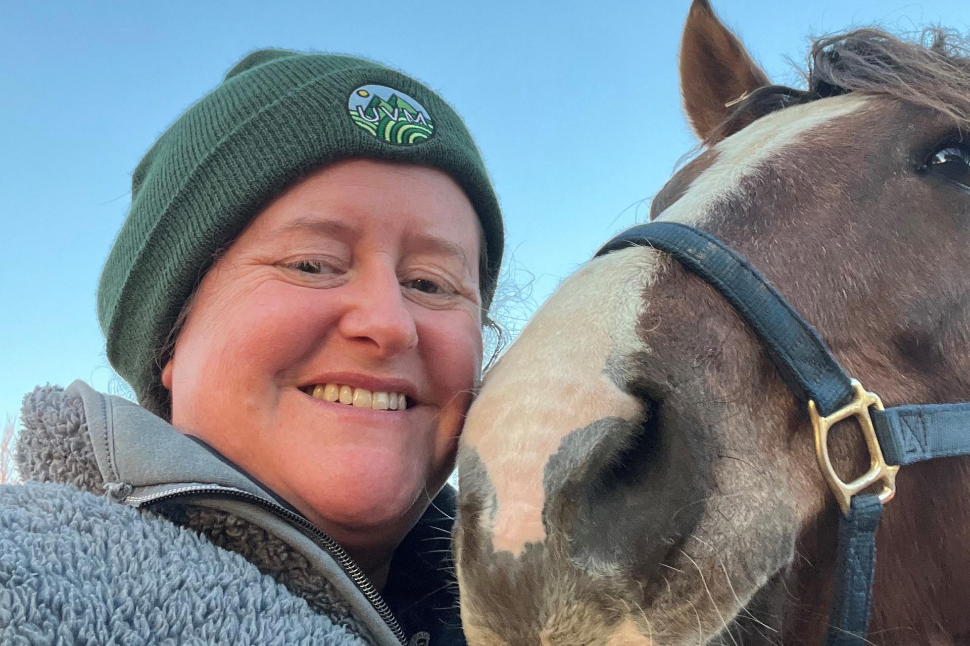 close-up of woman in gray fleece and green knit cap with her horse