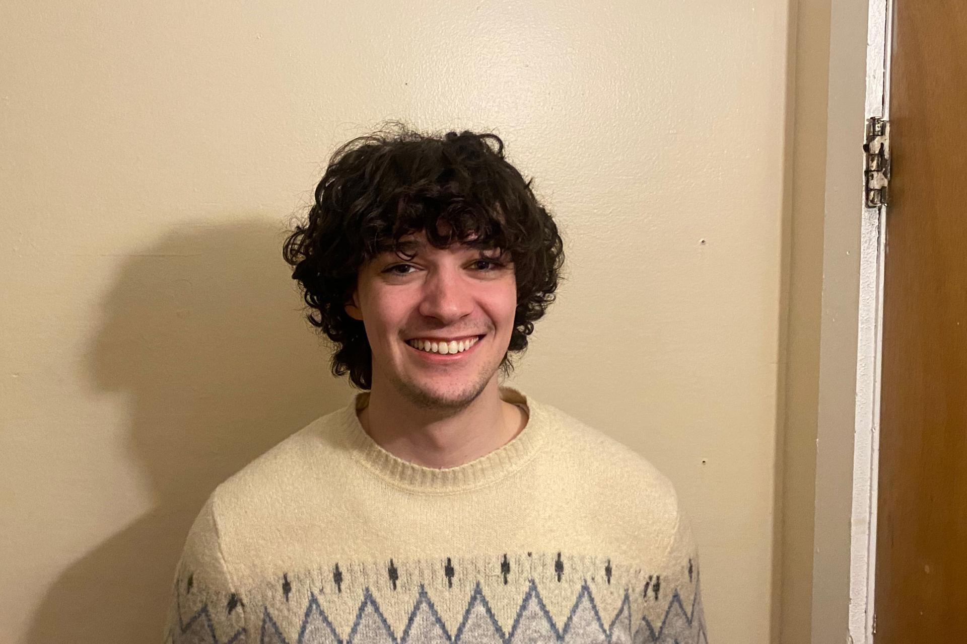 Student Iain Pless standing in front of beige wall smiling