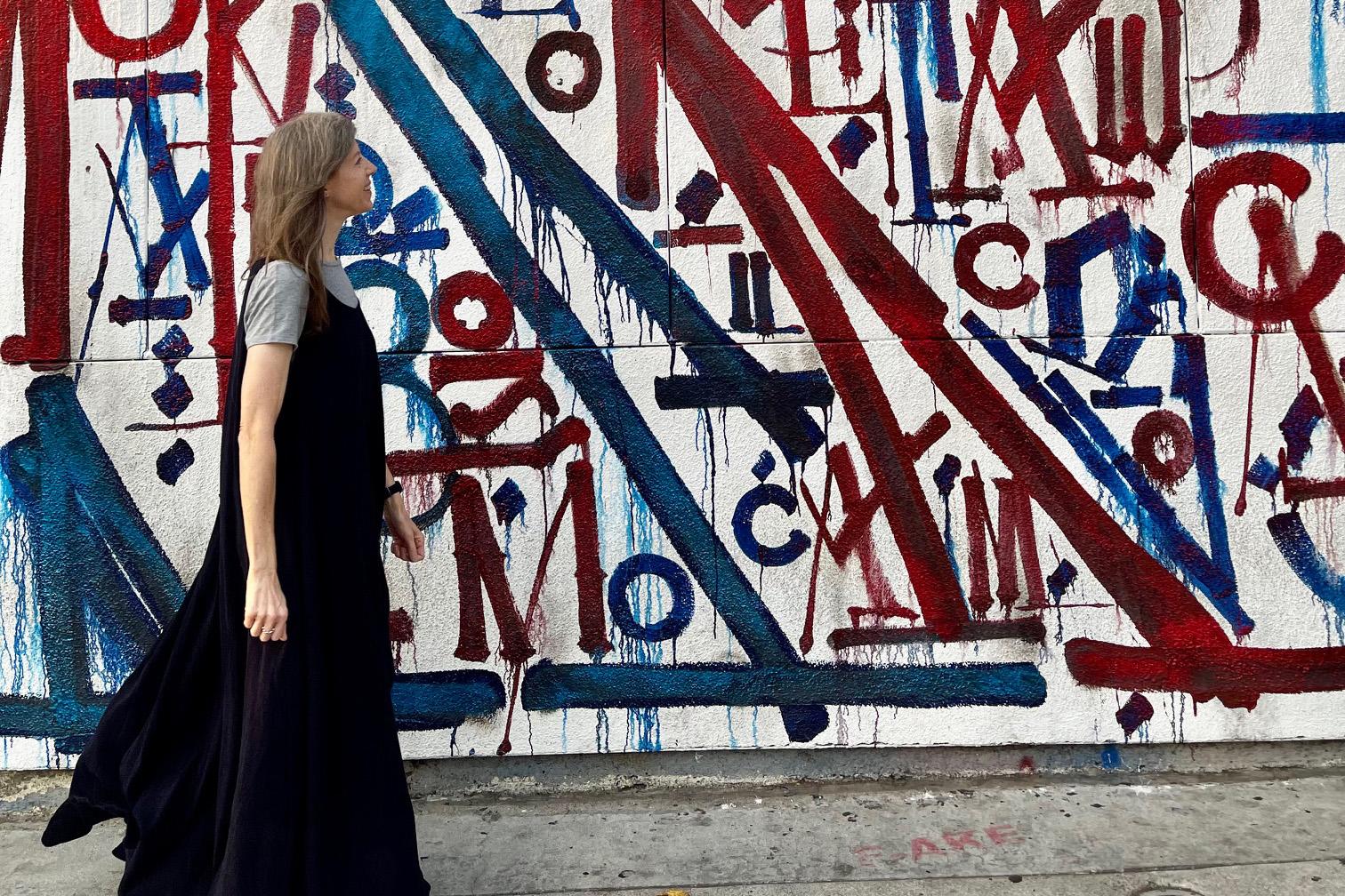 woman in profile wearing black dress walking past wall painted with graffiti art