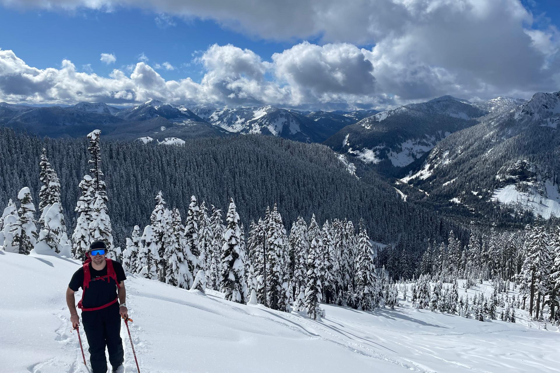 man with red backpack on skis in snow with mountains in background