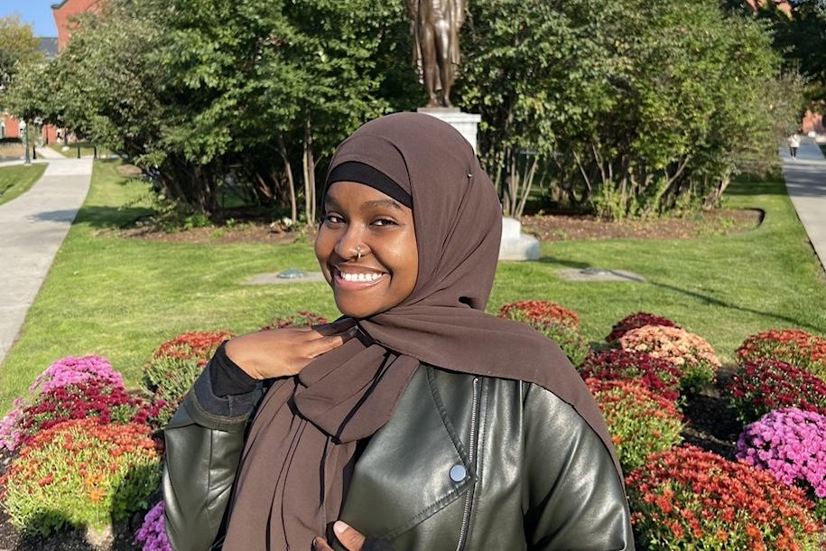 Halima Said smiling on campus in front of Ira Allen statue on the University Green.