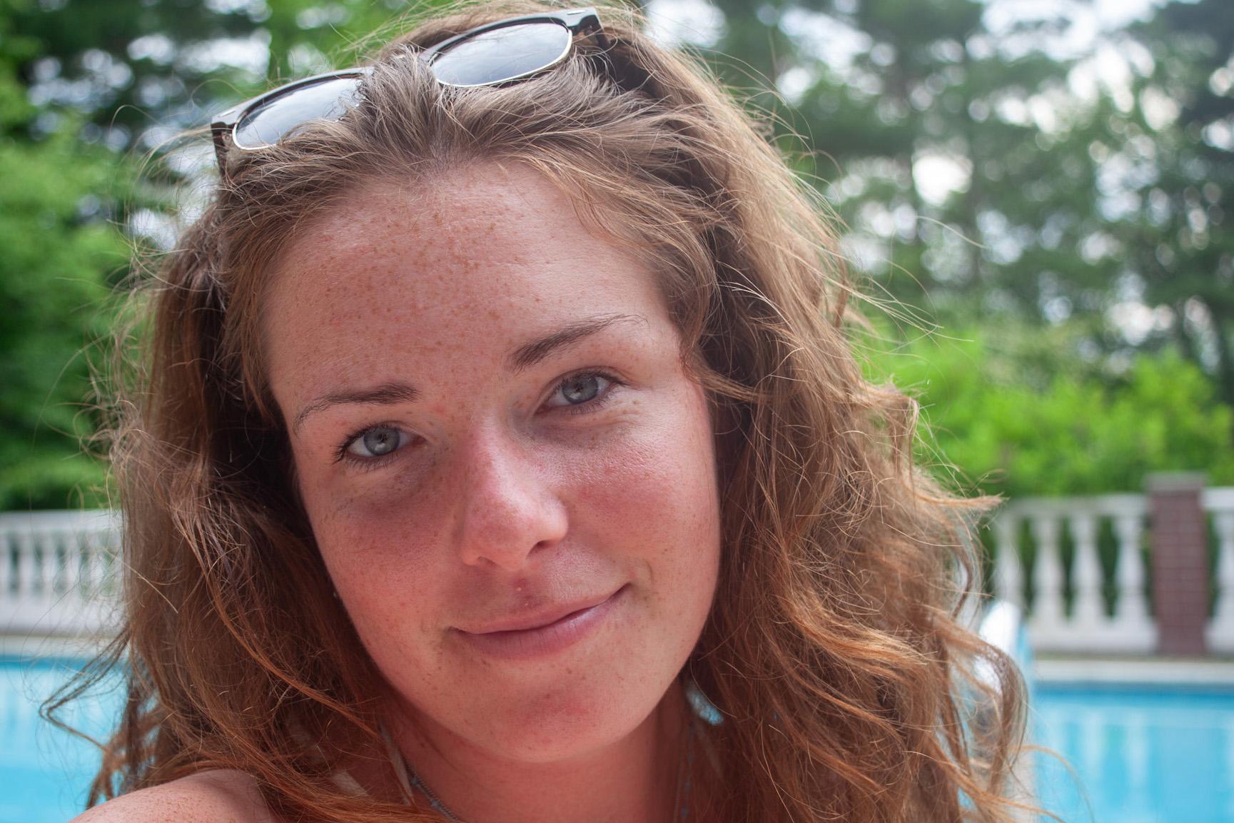 close-up of young woman with wavy light brown hair and sunglasses perched on head, by the pool