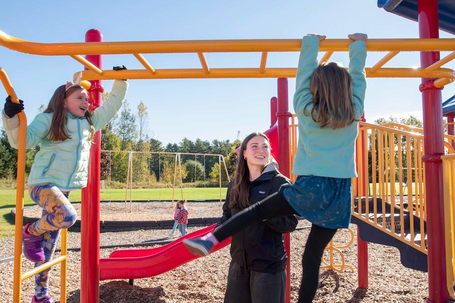 Ella McCarthy with two students outside on the playground at Essex Elementary School