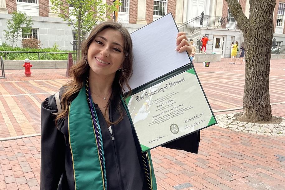 Sarah Bloch dressed in regalia on Church Street holding her diploma