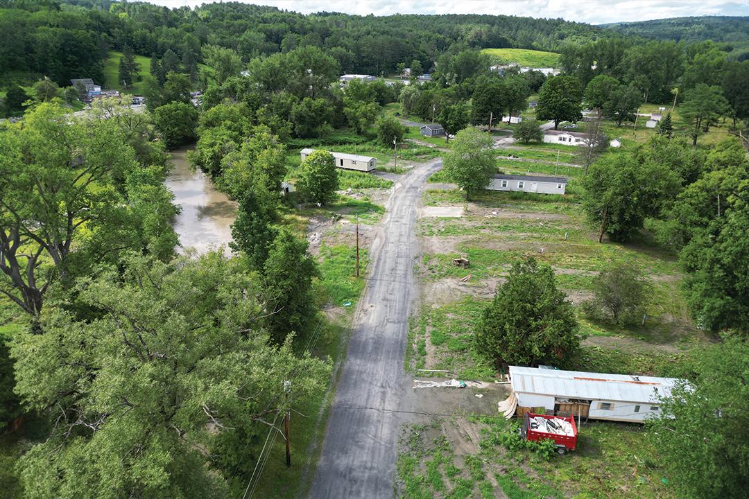 a vermont landscape featuring a river, dirt road, and three mobile home units