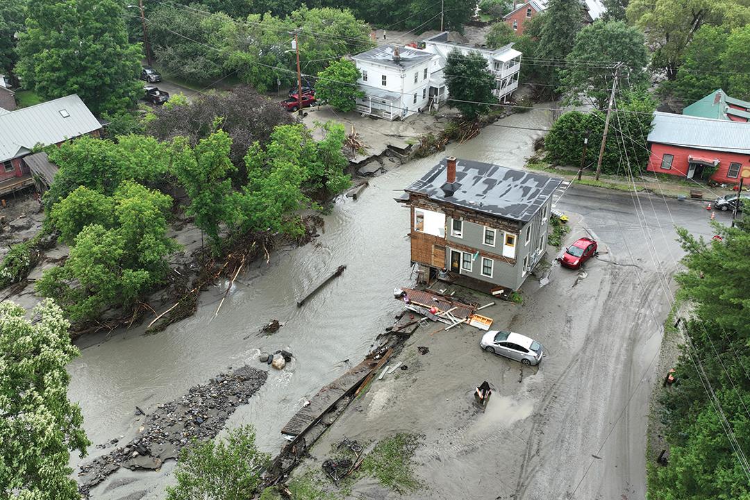 a severely damaged building teeters over a flooded river with lots of rocks and debris.