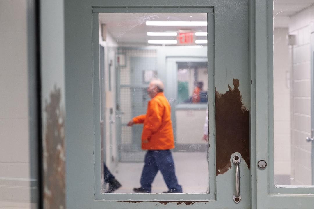 the sillouette of a person in an orange prison jumpsuit through the window of a prison security door