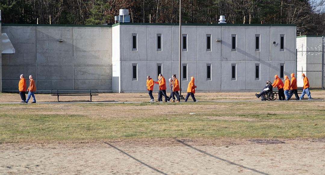 a group of prisoners in an orange jumpsuit walk across a prison yard