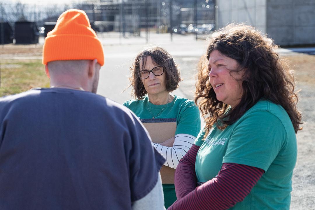 a person in an orange winter hat talks to two people wearing green shirts
