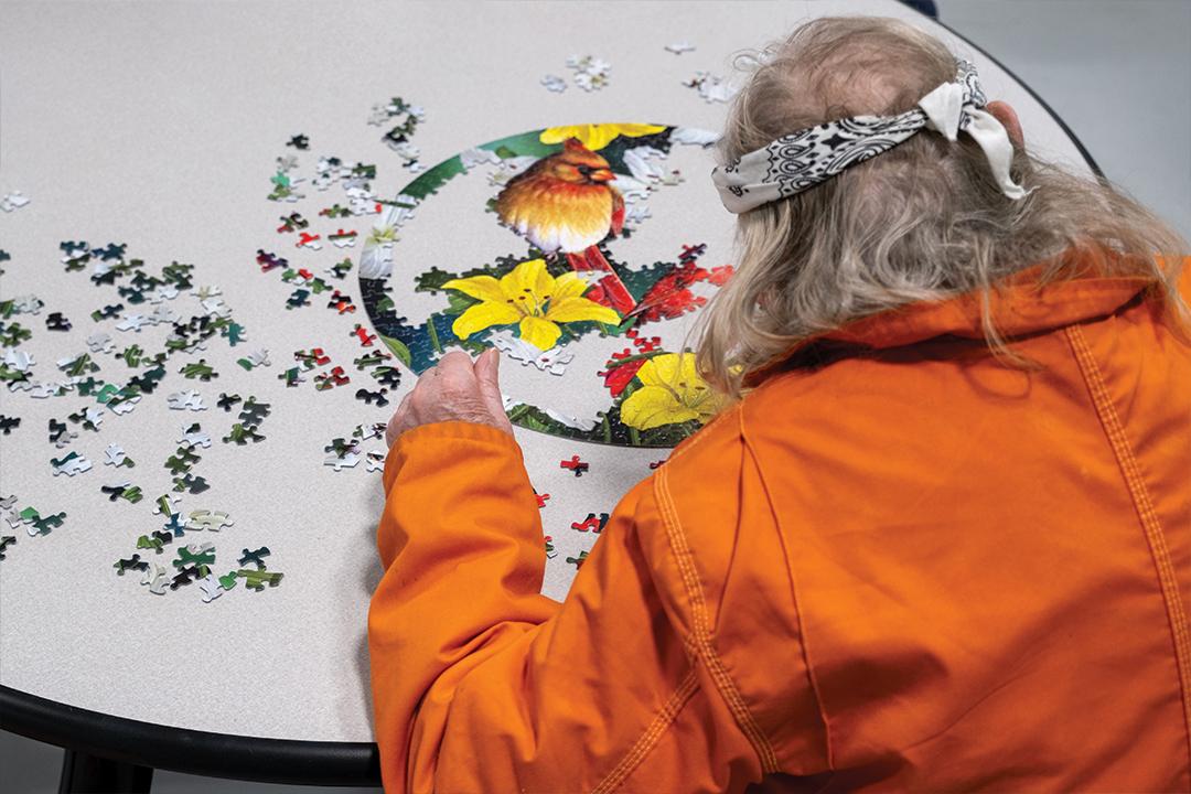 an inmate wearing a bandana and orange jumpsuit works on a puzzle of flowers