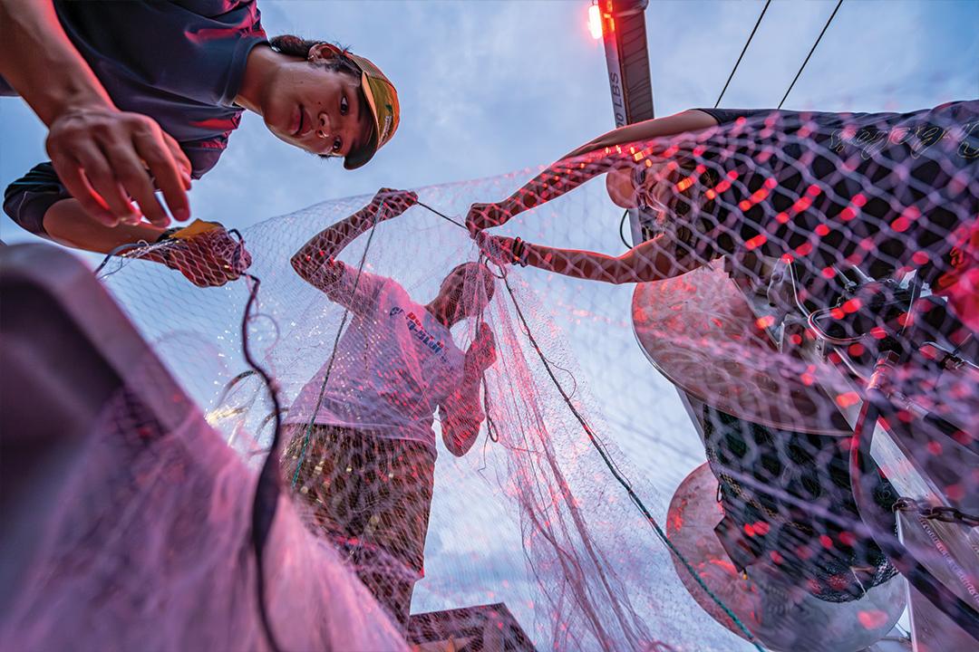 three students pull a red net against a dusk sky
