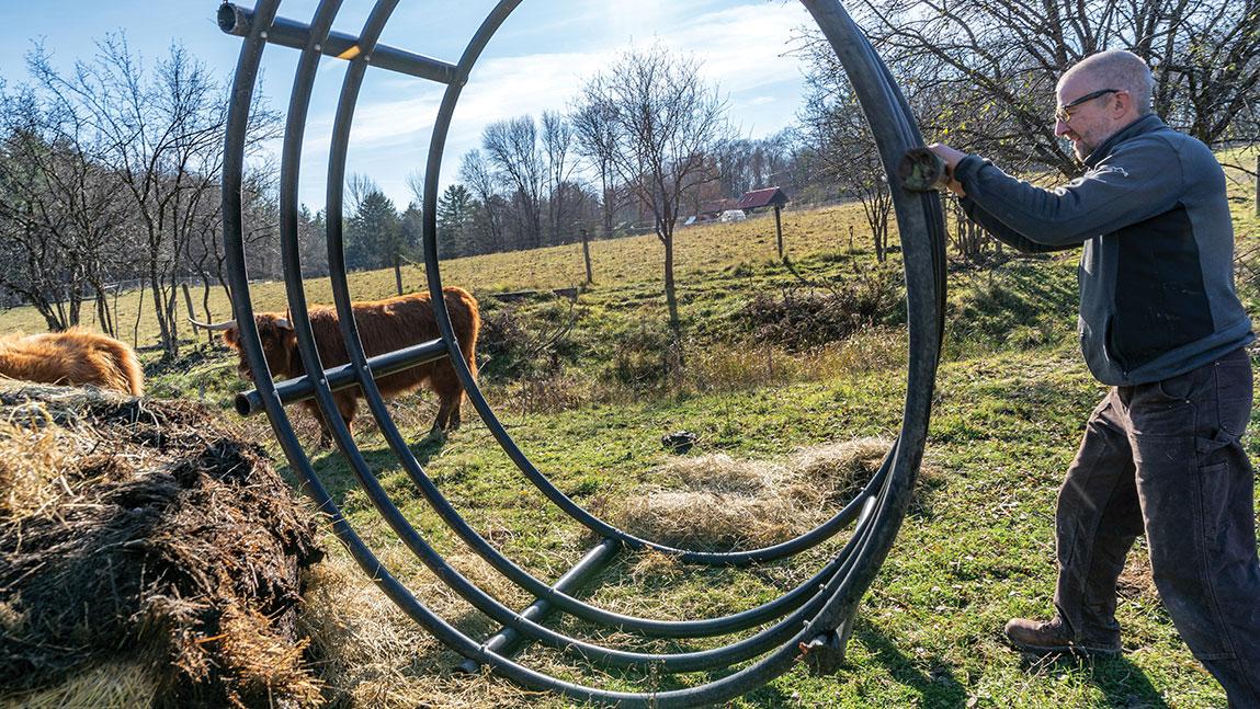 mark usher pushes a giant hay bail hoop in a farm field