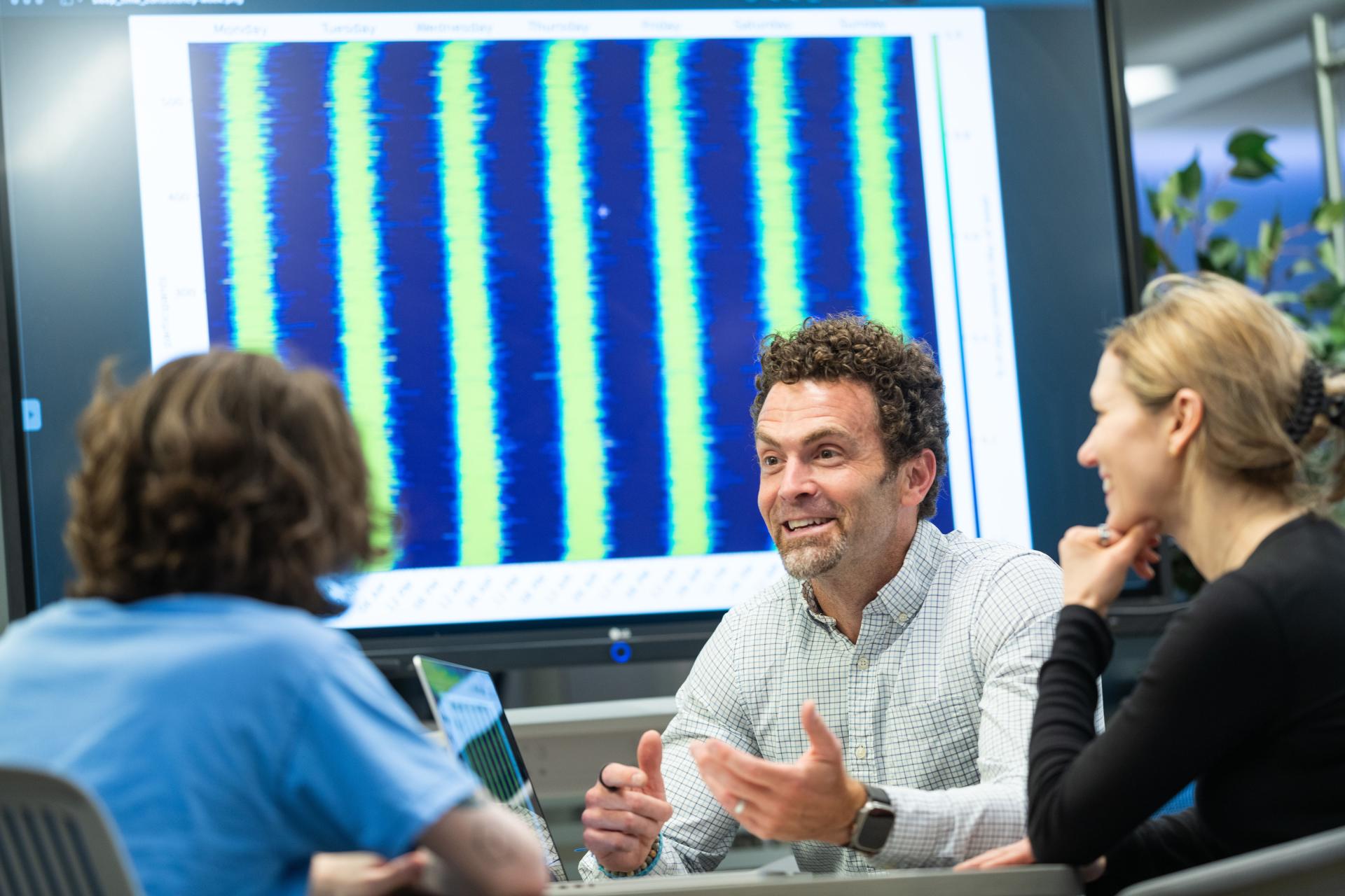 three researchers sit at a table reviewing data on a screen