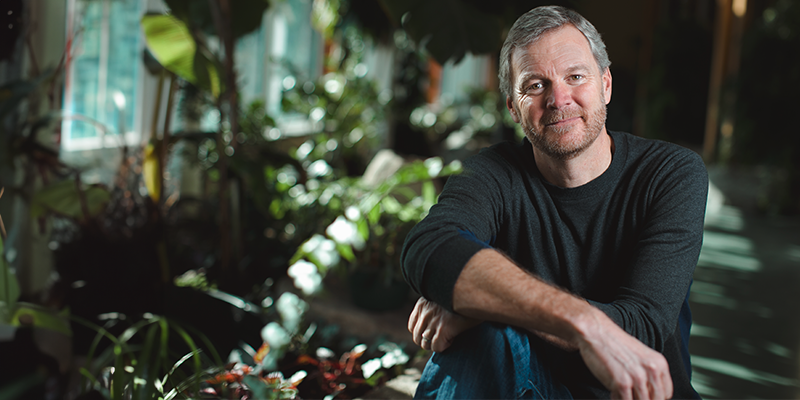 taylor ricketts smiling at the camera with his arms crossed surrounded by plants