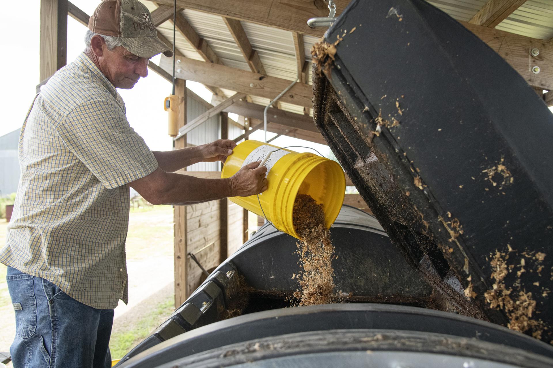 A man dumps food scraps from a bucket into a larger composter. 