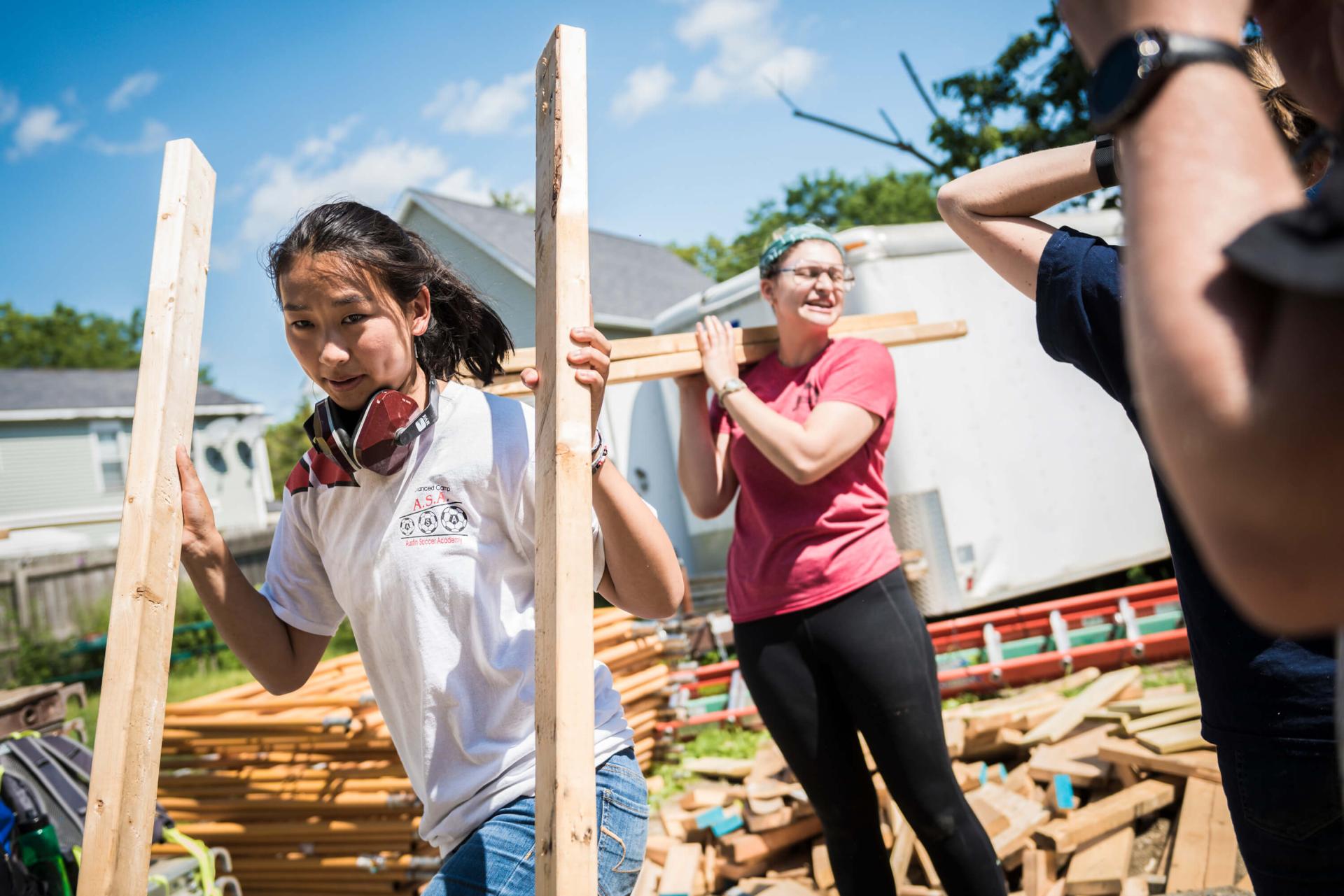 A UVM student carries two pieces of lumber during a building project