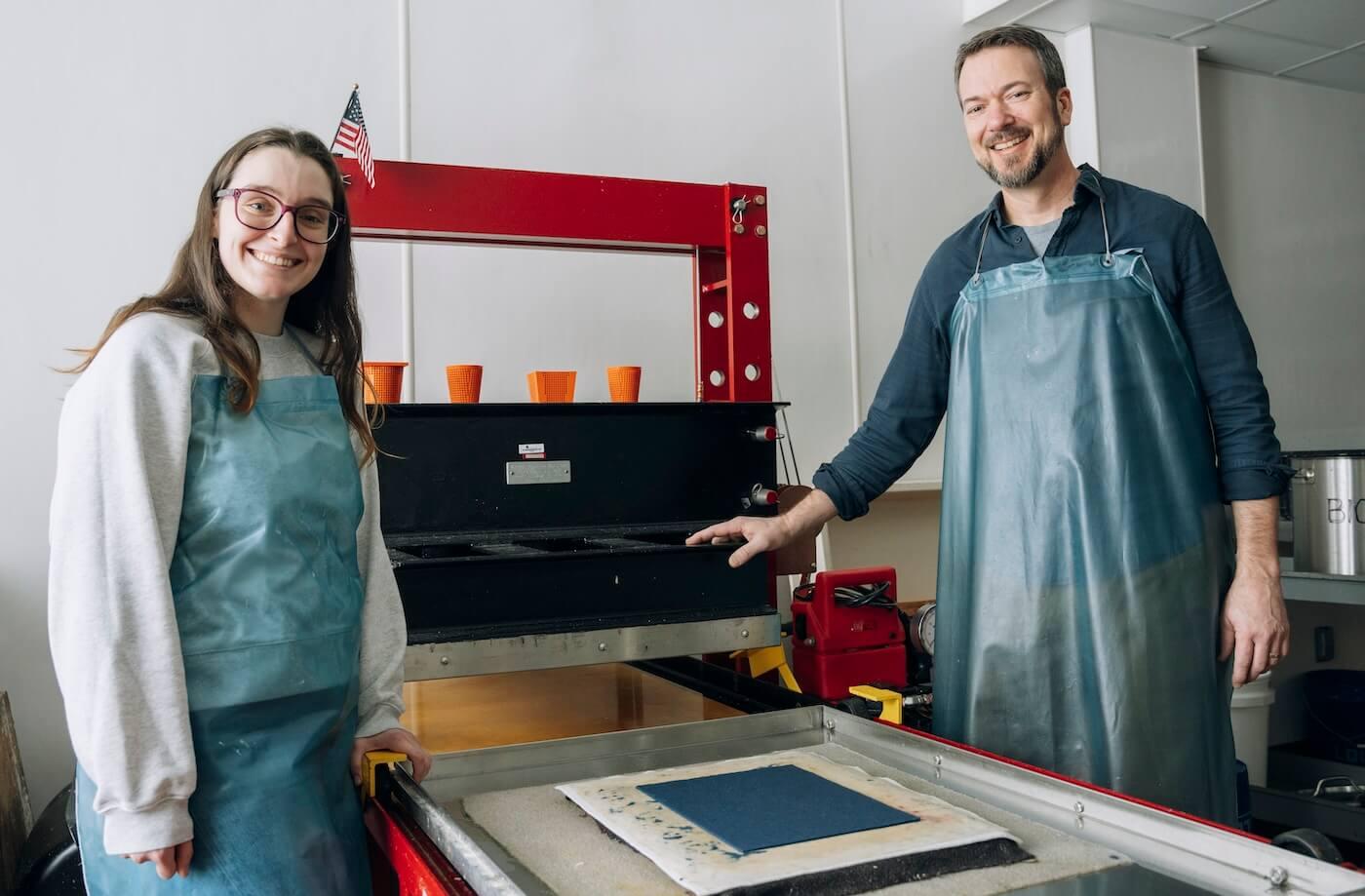 Student and faculty standing in front of a machine in the biofiber lab