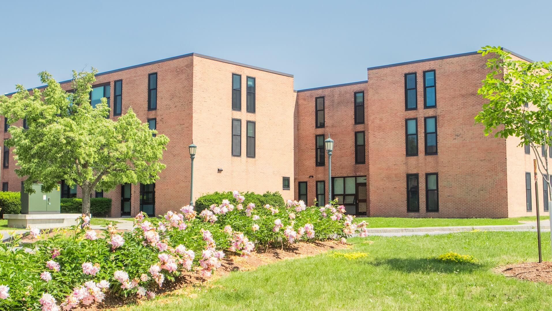 A brick three-story building with flowers and a grassy area.