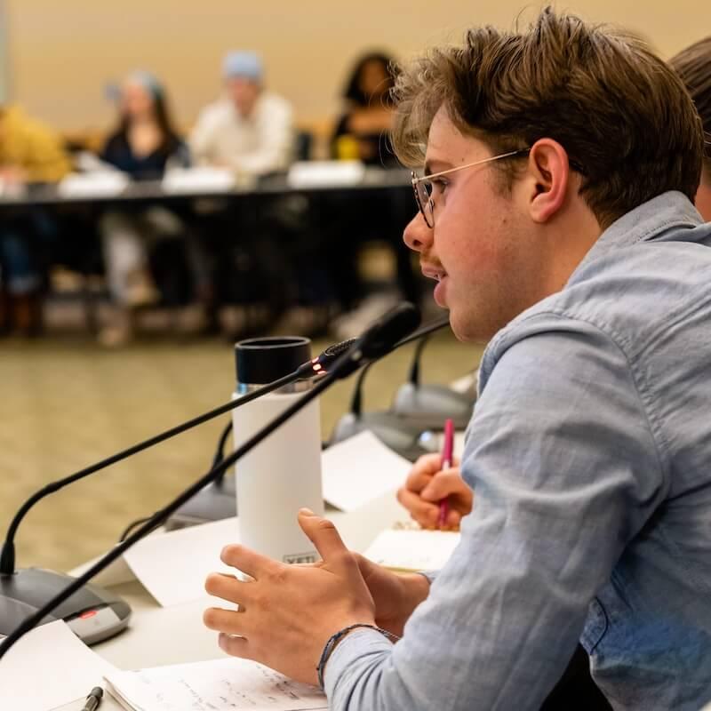 A student speaking into a microphone at a meeting.