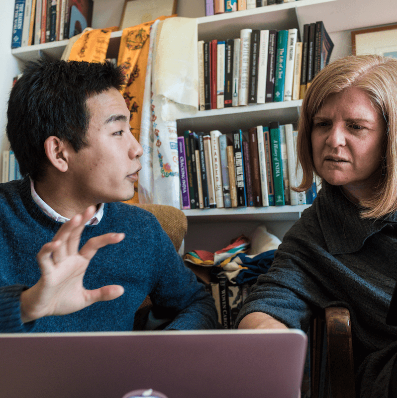 Student and professor chat and look at a laptop screen