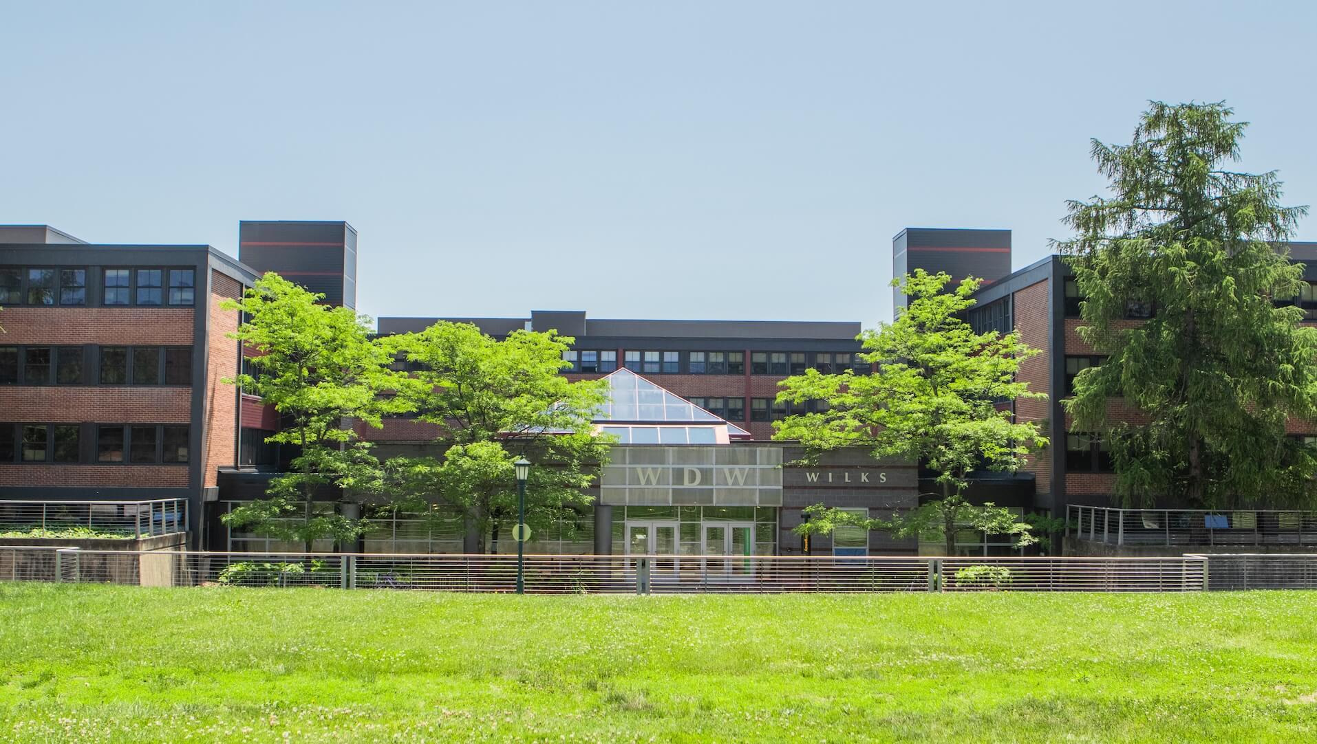 A brick, four-story building with a glass pyramid feature and a grassy area.