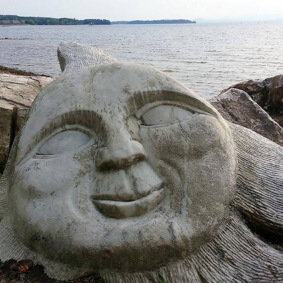 Smiling sun face carved into stone on shore of a lake