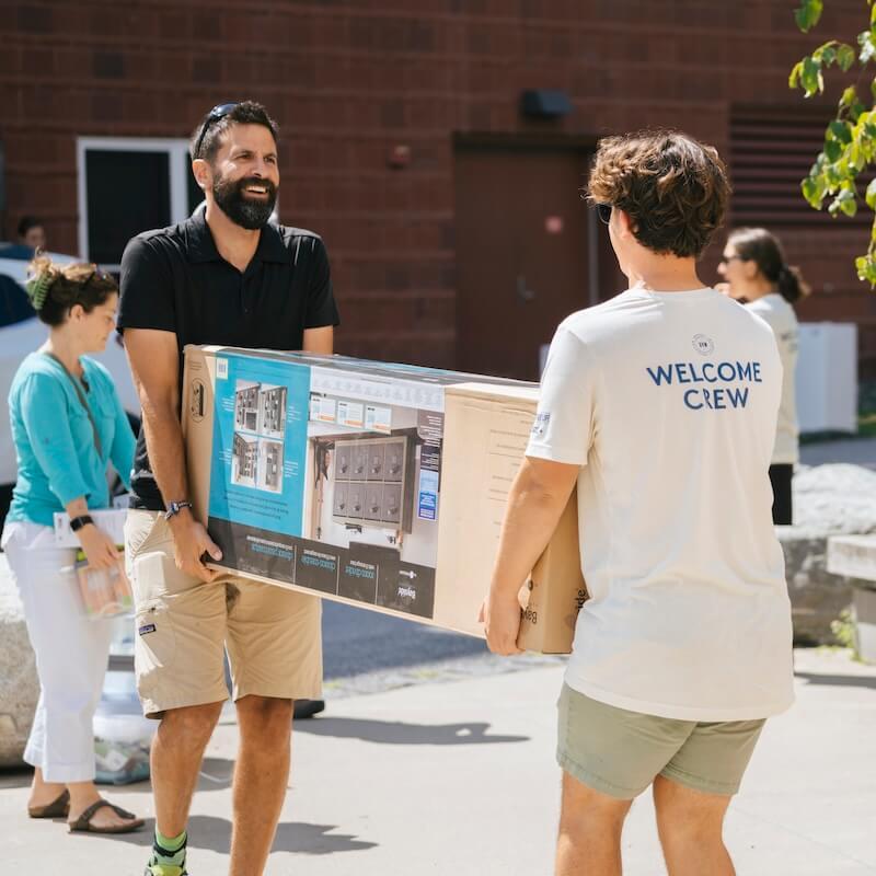 A parent and welcome crew member carry furniture into the residence halls.