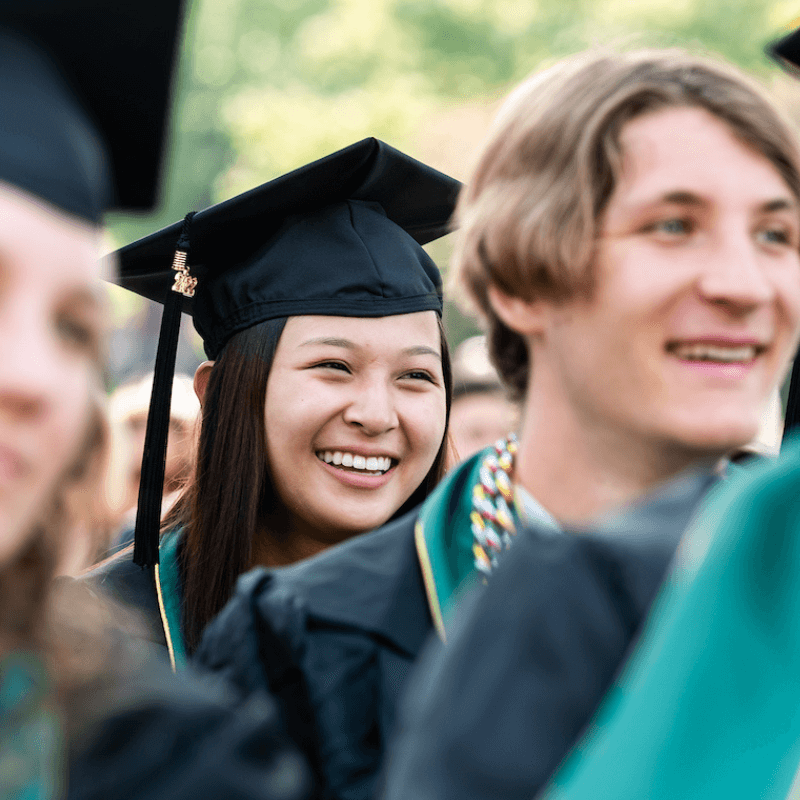 A student wearing cap and gown smiles during graduation